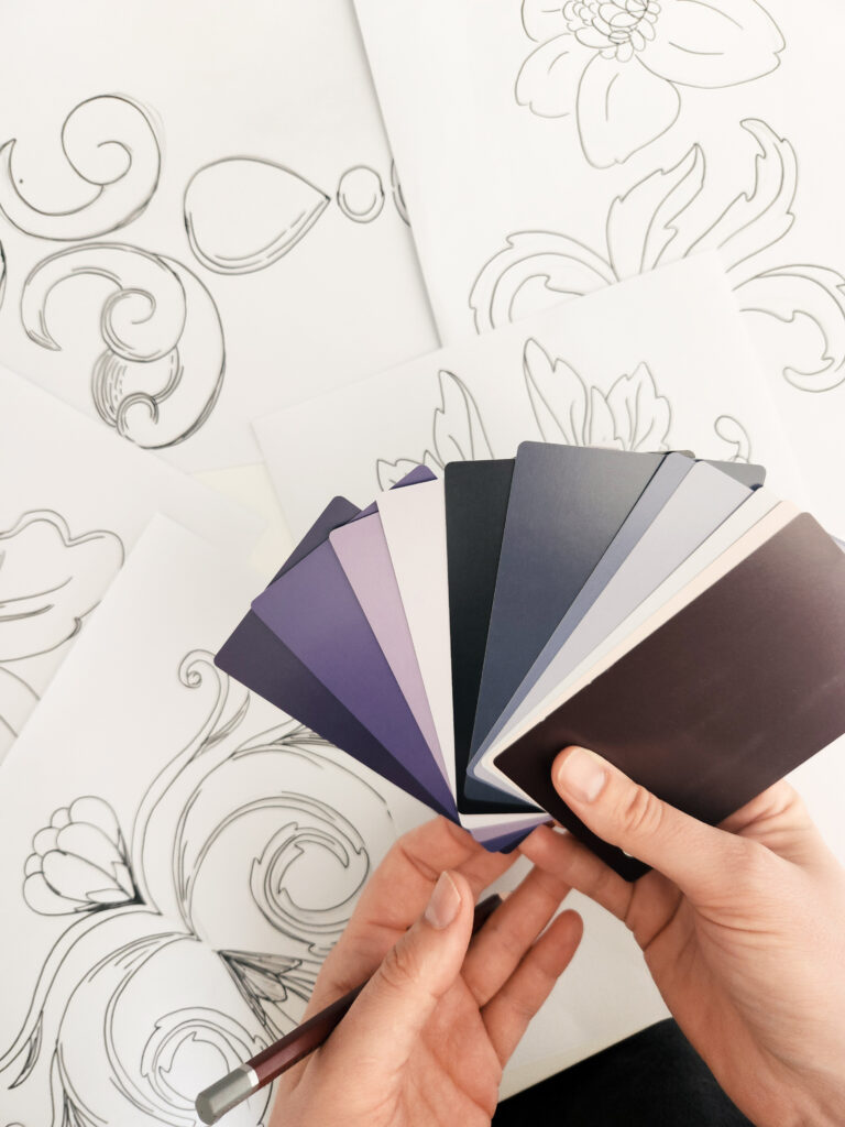 Surface pattern design color palette selection with moody purple and neutral swatches over hand-drawn floral motif sketches