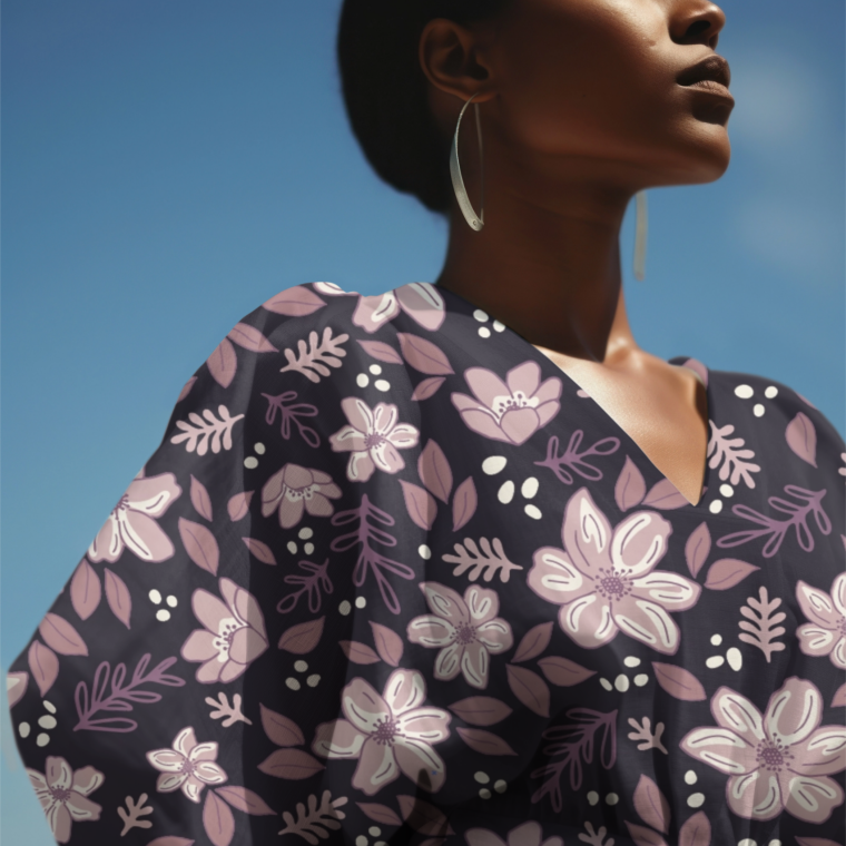 Model wearing a purple V-neck dress with puff sleeves, printed with hand-drawn mauve and cream florals and leafy motifs, photographed against a blue sky.